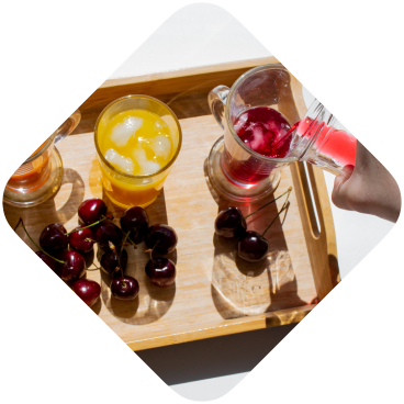 A wooden tray with colorful drinks: orange, yellow, and cucumber lemonade.